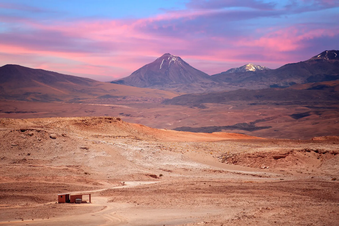 Paisaje volcánico de Atacama bajo un cielo de tonos rosados.