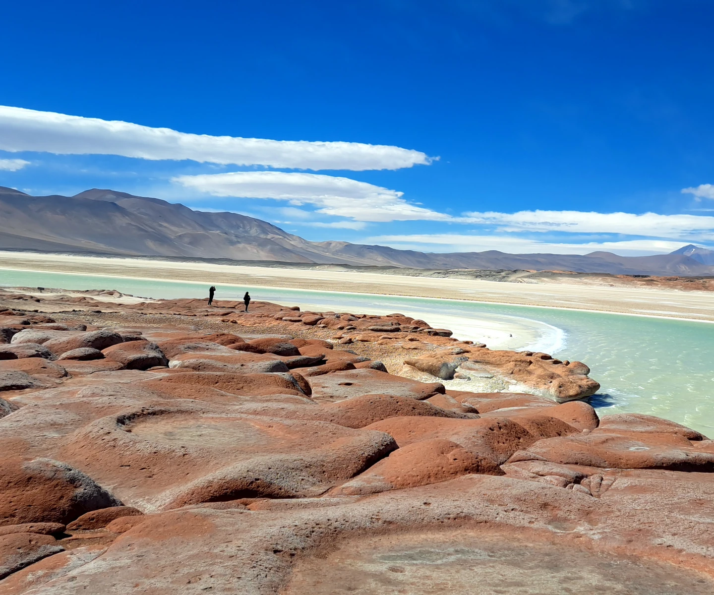 Rocas rojizas junto a una laguna de Piedras Rojas, con montañas al fondo.